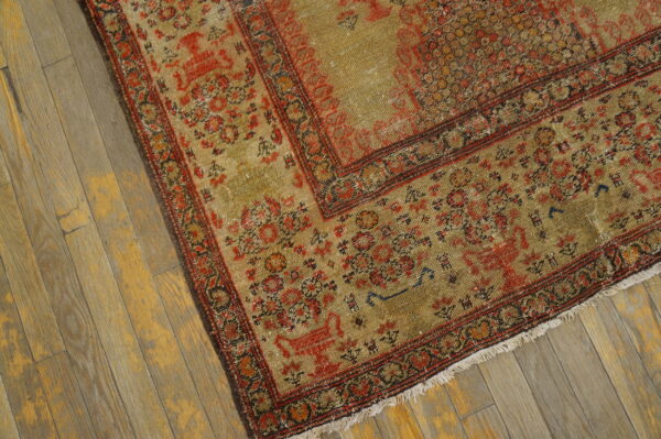 Distressed khaki and red patterned rug with fringe resting on worn yellow wood planks.