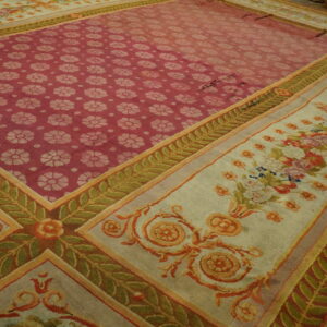 Large low-pile rug with a red-pink repeating floral center and multi-layered cream and green patterned borders.