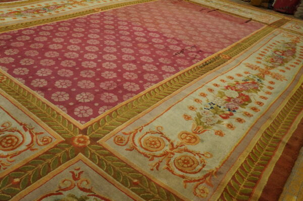 Large low-pile rug with a red-pink repeating floral center and multi-layered cream and green patterned borders.
