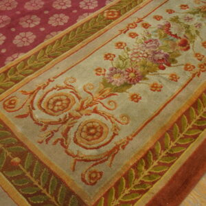 Intricate floral rug featuring a sage panel with a bouquet and deep red medallion border on wood planks.