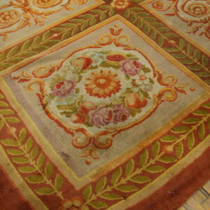 Ornate floral rug with beige ground, terracotta borders, and green vines resting on hardwood flooring.