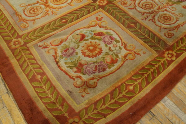 Ornate floral rug with beige ground, terracotta borders, and green vines resting on hardwood flooring.