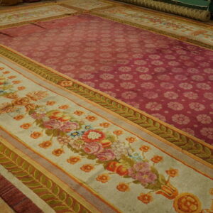 Ornate rug showing a maroon field of repeating flowers and a cream border with multicolored floral bouquets on wood floor.