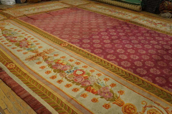 Ornate rug showing a maroon field of repeating flowers and a cream border with multicolored floral bouquets on wood floor.