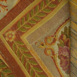 Tightly woven rug featuring rust, olive, and gold botanical borders rests on warm plank wood flooring.