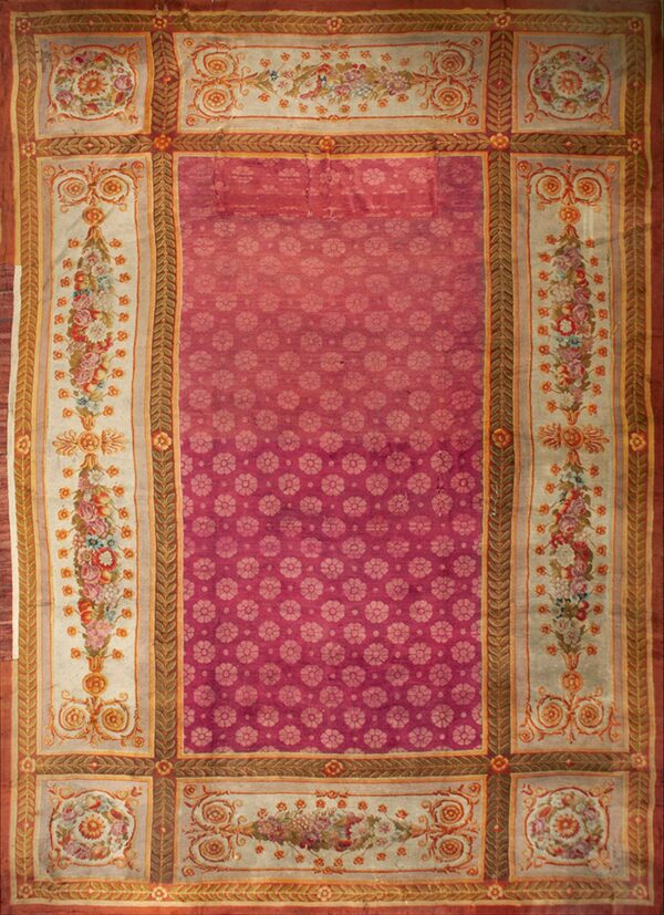 A magenta rug with an allover repeating small floral pattern and a wide ivory border with colorful bouquets.