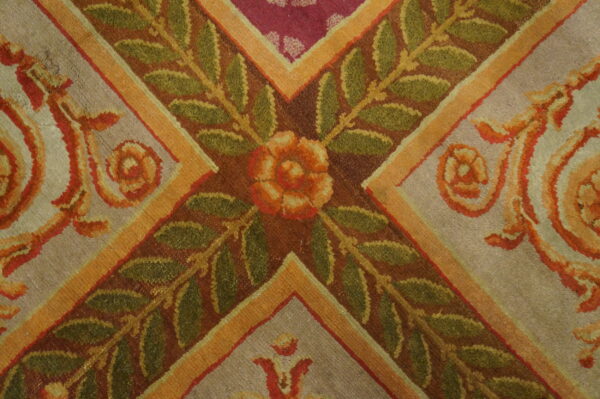Textured rug close-up shows green leaves, an orange flower, gold stripes, and grey and magenta background panels.
