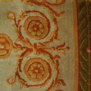 Close-up shows scrolling orange and red floral motifs on a light field, bordered by green leaves on maroon.