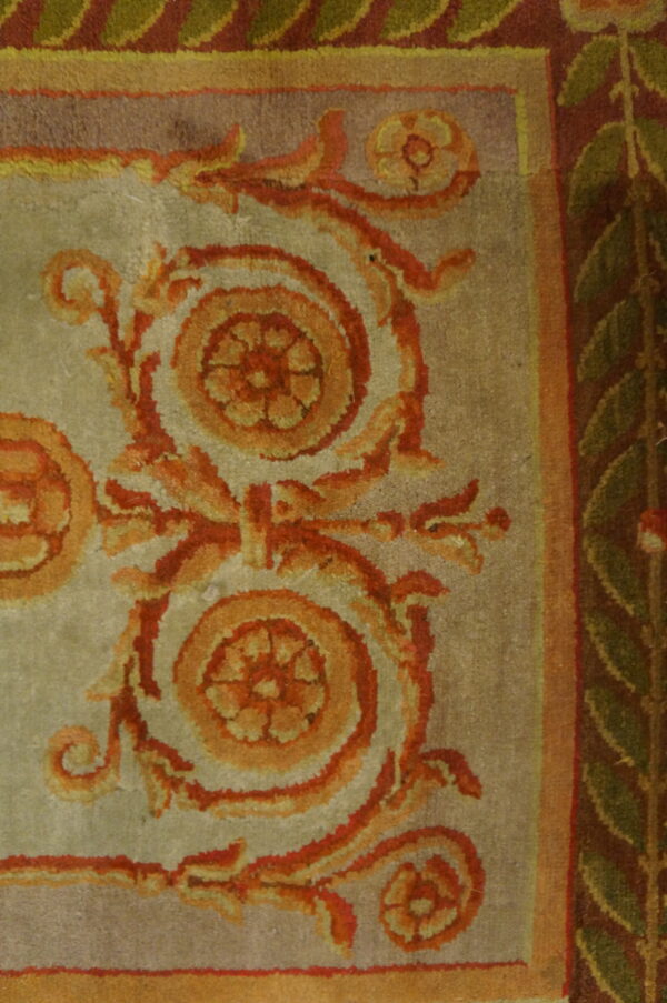 Close-up shows scrolling orange and red floral motifs on a light field, bordered by green leaves on maroon.