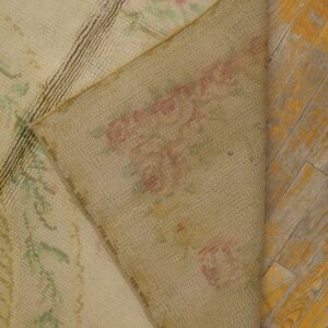 Cream high-pile rug with pink and green floral designs flipped over on weathered yellow hardwood.