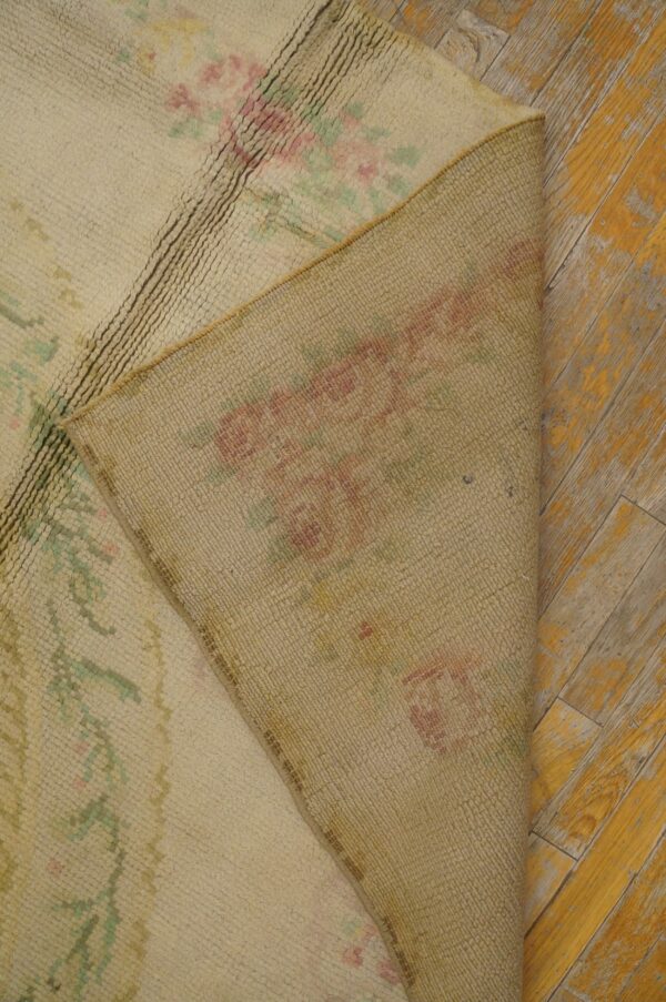 Cream high-pile rug with pink and green floral designs flipped over on weathered yellow hardwood.