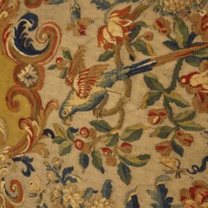 Muted flatweave detail with a parrot, red roses, and scrolling blue patterns on a pale tan ground.