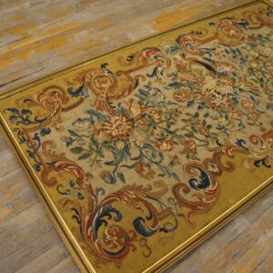 Low-pile rug with elaborate floral patterns and a gold frame rests on distressed yellow wood floorboards.