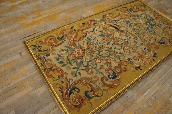 Low-pile rug with elaborate floral patterns and a gold frame rests on distressed yellow wood floorboards.