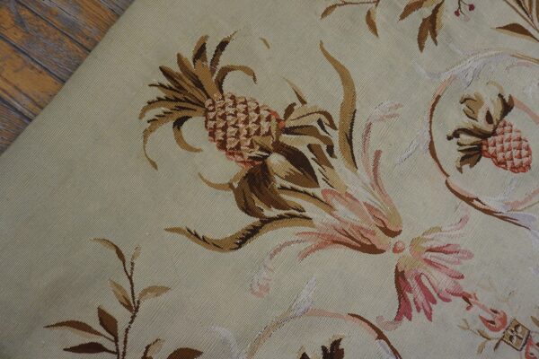 Tapestry-style beige rug displays ornate brown and pink pineapple and floral scrollwork near wood flooring.