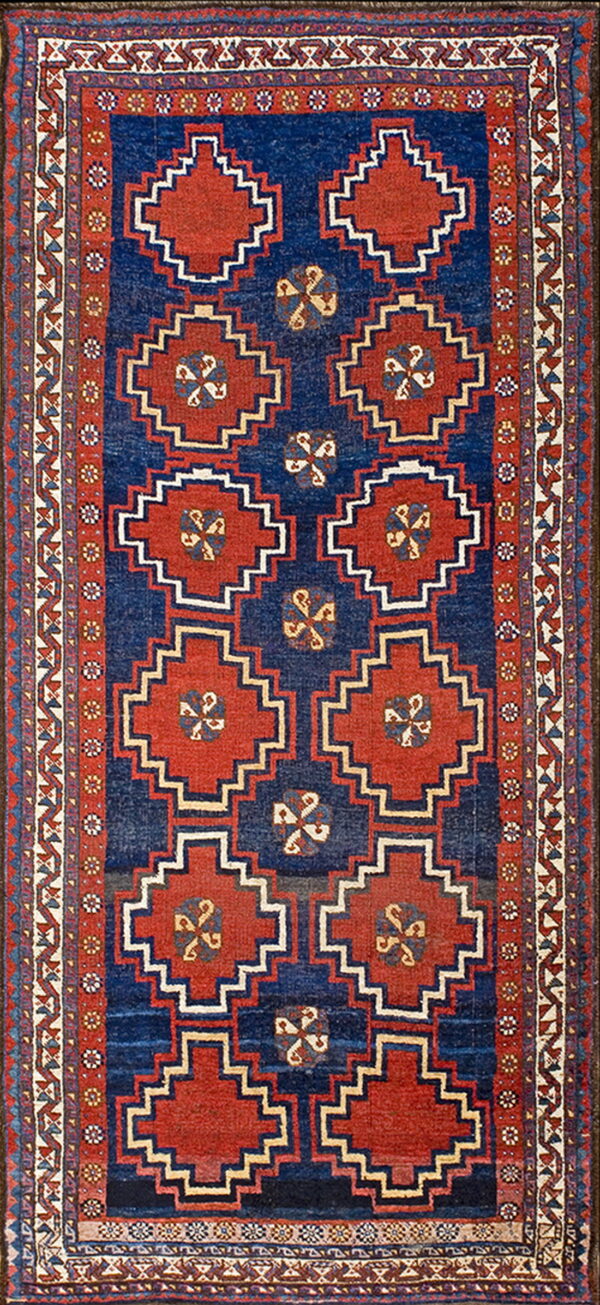 Blue and red rug with serrated diamond medallions and detailed geometric guard borders on a dark field.
