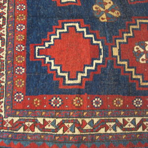 Low-pile blue, red, and cream rug corner displaying intricate geometric guls and borders with fringe.