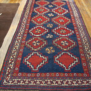 A red and blue runner with geometric designs lies on wood planks beside a plain brown rug.