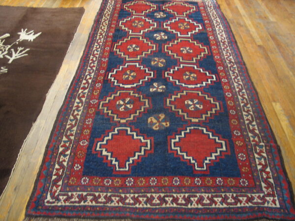 A red and blue runner with geometric designs lies on wood planks beside a plain brown rug.