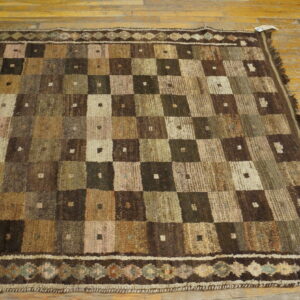 Low pile rug featuring a checkered design in earthy brown, beige, and green tones on wood plank flooring.