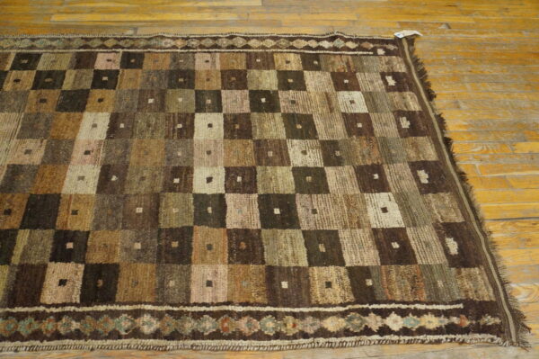 Low pile rug featuring a checkered design in earthy brown, beige, and green tones on wood plank flooring.