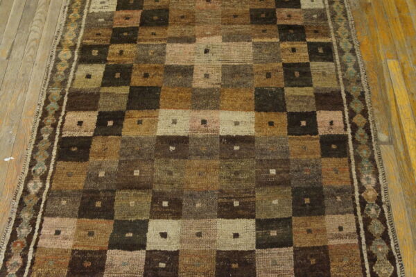 Muted brown and green runner rug with a geometric patchwork grid pattern and a detailed teal border on wood floor.
