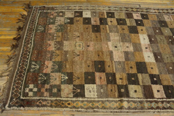 Textured rug with a brown and beige checkerboard pattern and geometric border on light wood flooring.