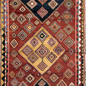 Textured burgundy rug featuring a complex geometric design of nested diamonds in black, gold, and accent colors.