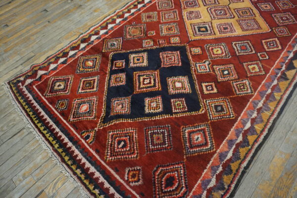 High-pile red rug with navy and gold blocks, filled with multicolor concentric square motifs, rests on gray wood flooring.
