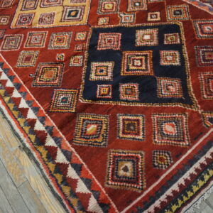 Red rug featuring colorful geometric squares and a dark blue center medallion on distressed gray wood flooring.