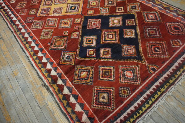 Red rug featuring colorful geometric squares and a dark blue center medallion on distressed gray wood flooring.