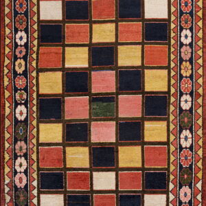A colorful rug with a rectangular grid pattern in navy, red, yellow, and cream, surrounded by floral borders.