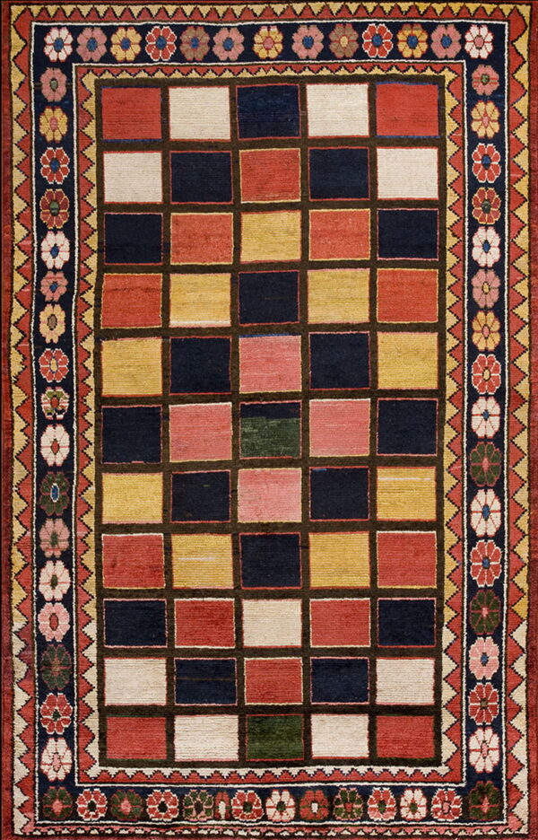 A colorful rug with a rectangular grid pattern in navy, red, yellow, and cream, surrounded by floral borders.