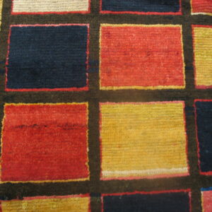 Close-up of a geometric rug featuring a grid pattern of red, yellow, and navy blocks with a zigzag border.