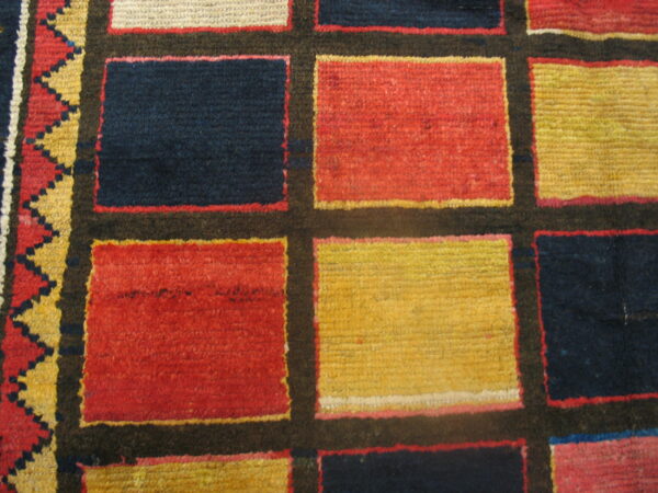 Close-up of a geometric rug featuring a grid pattern of red, yellow, and navy blocks with a zigzag border.
