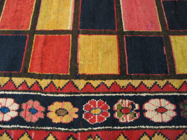 Vibrant geometric rug detail with large squares in red, yellow, and navy above a floral stripe border.