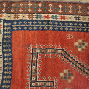 Rust-red field with stacked geometric borders in navy, brown, and cream; showing low pile texture.