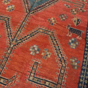 Close view of a rust red rug featuring complex geometric patterns, angular navy motifs, and a striped border.
