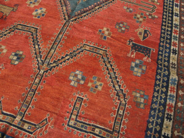 Close view of a rust red rug featuring complex geometric patterns, angular navy motifs, and a striped border.