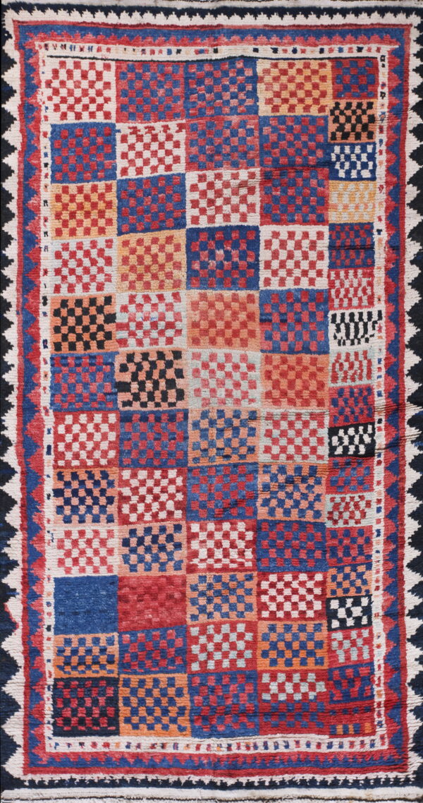 Textured rug featuring a bold checkerboard grid pattern in red, blue, orange, cream, and black, with geometric borders.