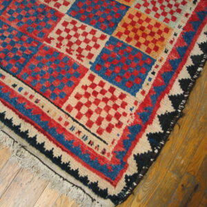 Geometric rug with large checkerboard blocks in red, blue, and orange rests on light brown hardwood.