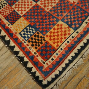 Multicolored rug with checkerboard diamond patterns and fringe shown on weathered wood floor.