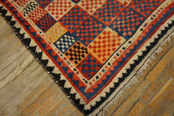 Multicolored rug with checkerboard diamond patterns and fringe shown on weathered wood floor.