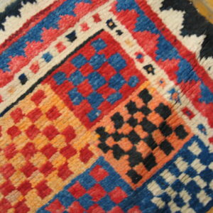 High-pile rug corner showing checkered geometric blocks in vibrant red, blue, orange, black, and cream.