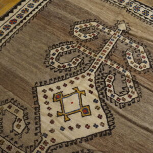 Geometric brown rug with cream, black, and multicolored tribal motifs resting on glossy wooden plank flooring.
