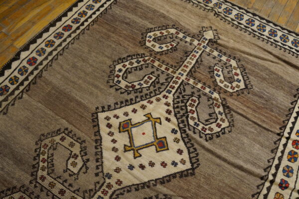 Geometric brown rug with cream, black, and multicolored tribal motifs resting on glossy wooden plank flooring.