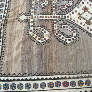 Close-up of a brown and gray rug with geometric tribal patterns, colorful rosette borders, and wood flooring visible.
