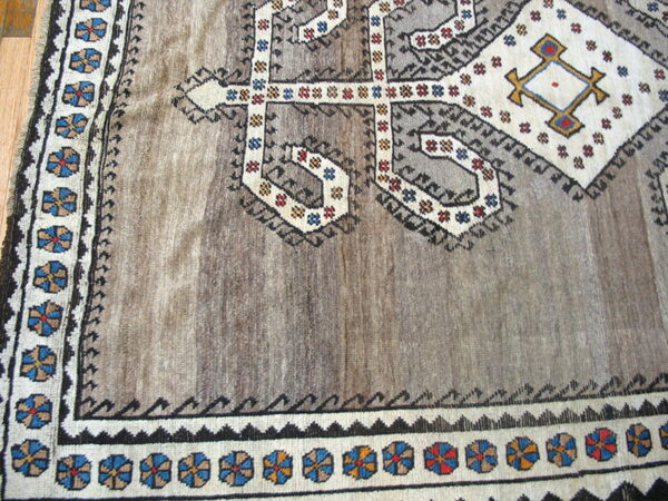 Close-up of a brown and gray rug with geometric tribal patterns, colorful rosette borders, and wood flooring visible.