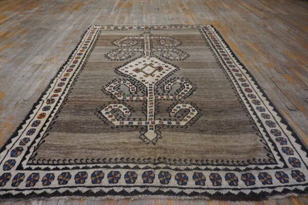 Grayish-brown geometric rug with a cream central medallion and multi-colored border on distressed wood floors.