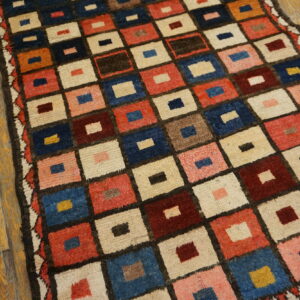 High-pile rug with a checkered design of red, blue, and cream squares over rustic wood flooring.